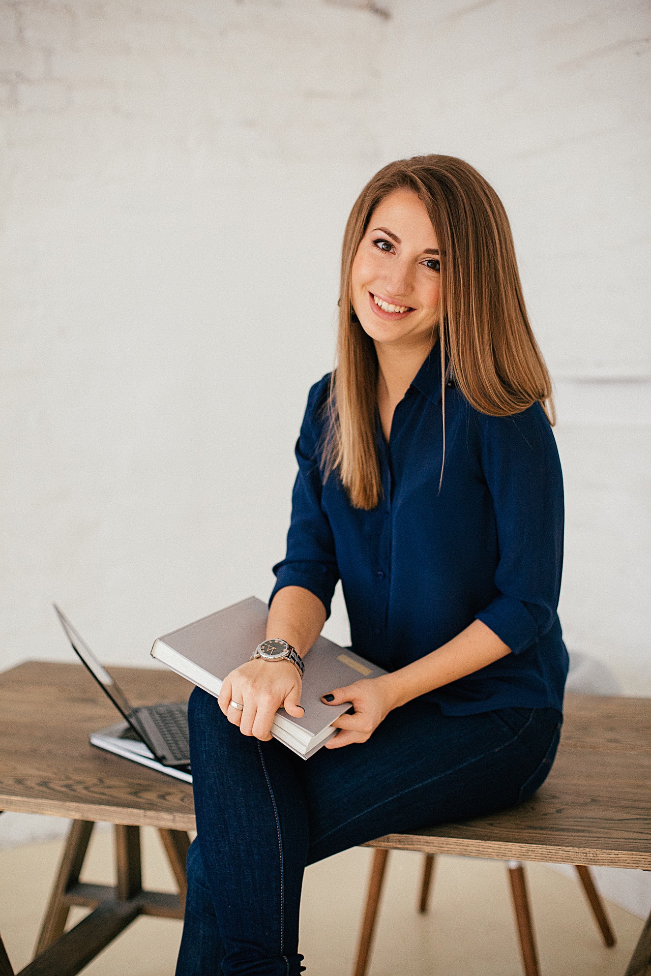 woman smiling sitting on desk holding a book